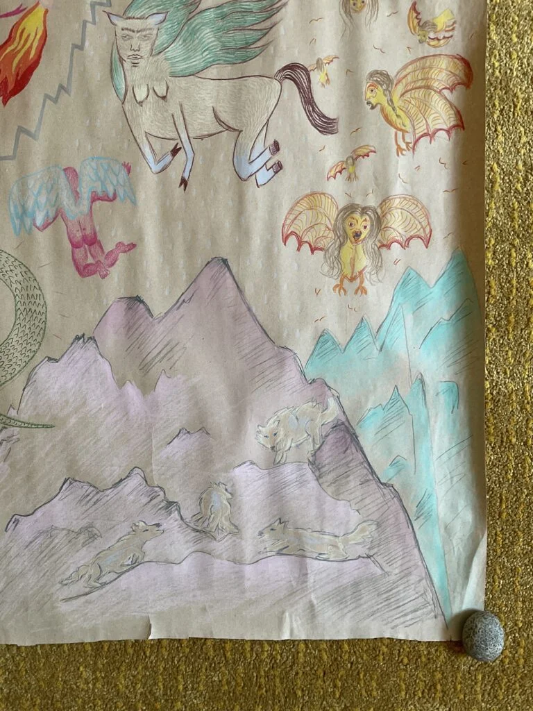 Dessin sur papier craft brun de forme carré au crayon de bois de couleurs. La scène montre des dragons dans le ciel, une créature ailée, un nuage fâché et des sirènes volantes surplombant un lac au fond duquel un enfant semble dormir, une montagne mauve avec des loups blancs et gris et des montagnes turquoises.