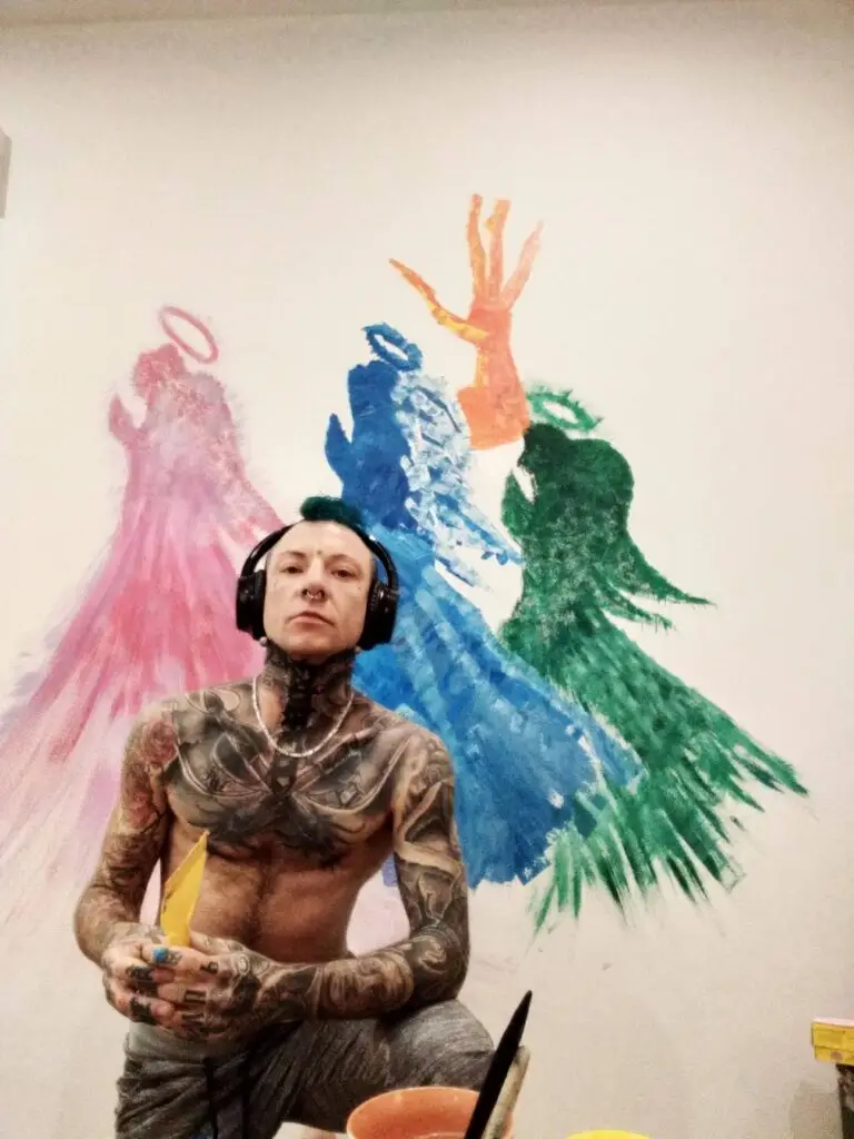 Mur avec peinture colorée abstraites devant Fattal avec une spatule en main écouteurs torse nu tatoué. Peau blanche.